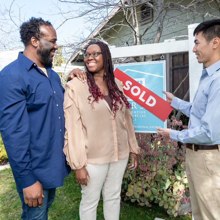 A man and woman stand in front of their recently purchased home and discuss home insurance inspections with their realtor.