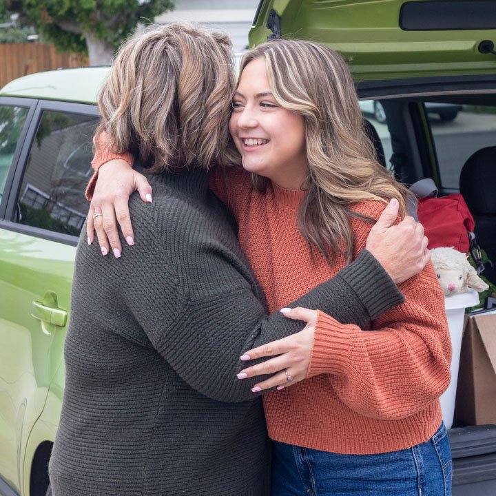 A daughter and mother hug outside a car that is better protected by the TruStage Auto and Home Program.