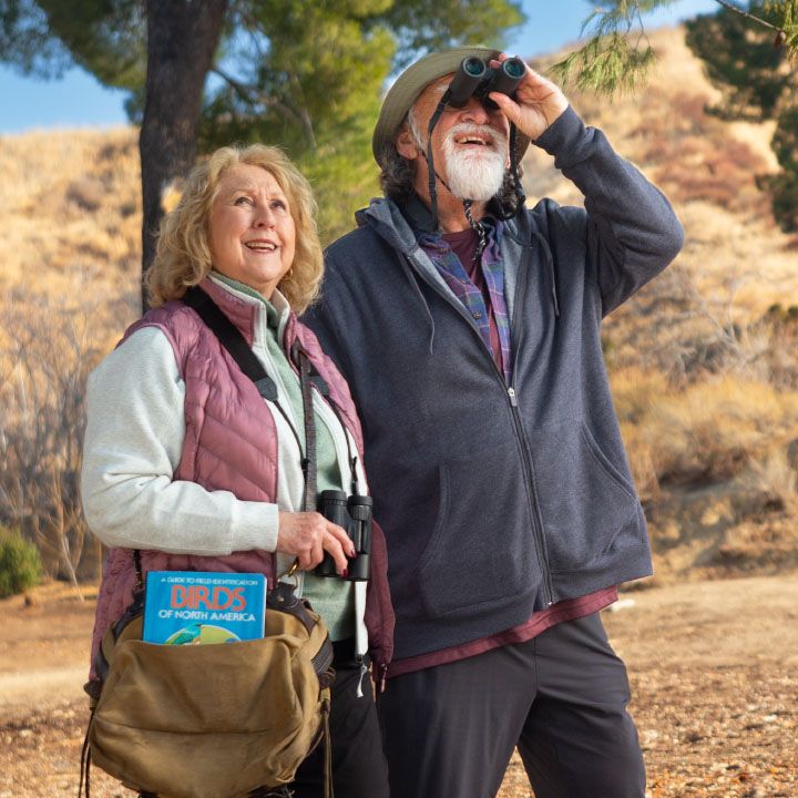 An older couple better protected by TruStage Insurance are birdwatching in the hills.