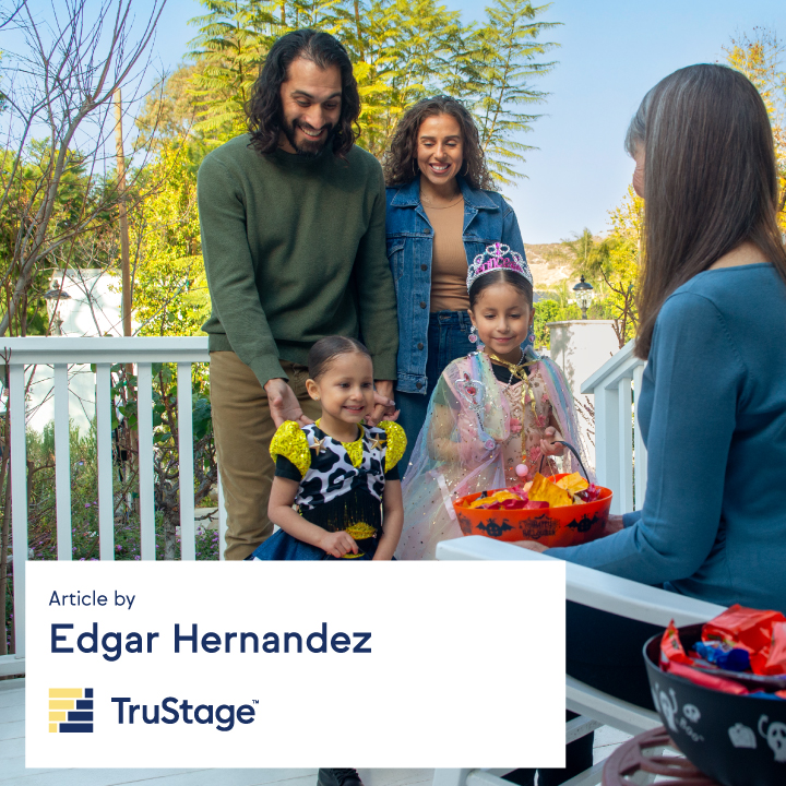 A mother and father stand on a front porch with their daughters dressed up for Halloween.