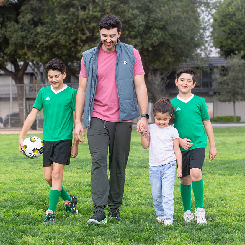 A father walks on a soccer field with his children smiling knowing he's protected with TruStage Term Life Insurance